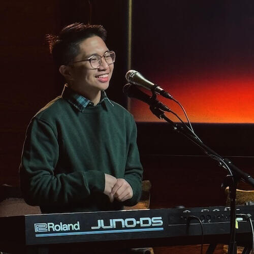 Lucas Tecson smiling behind a piano keyboard and microphone
